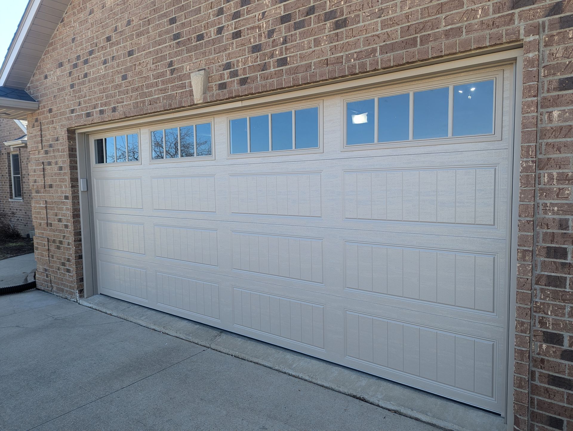 White garage door with small windows on a brick house, viewed from the driveway