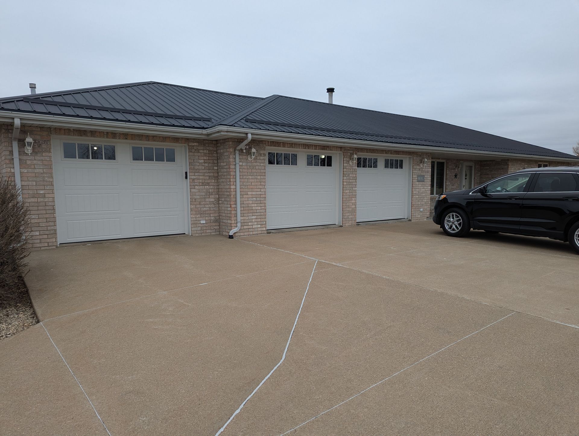 Brick house with three garage doors and a black SUV parked in the driveway