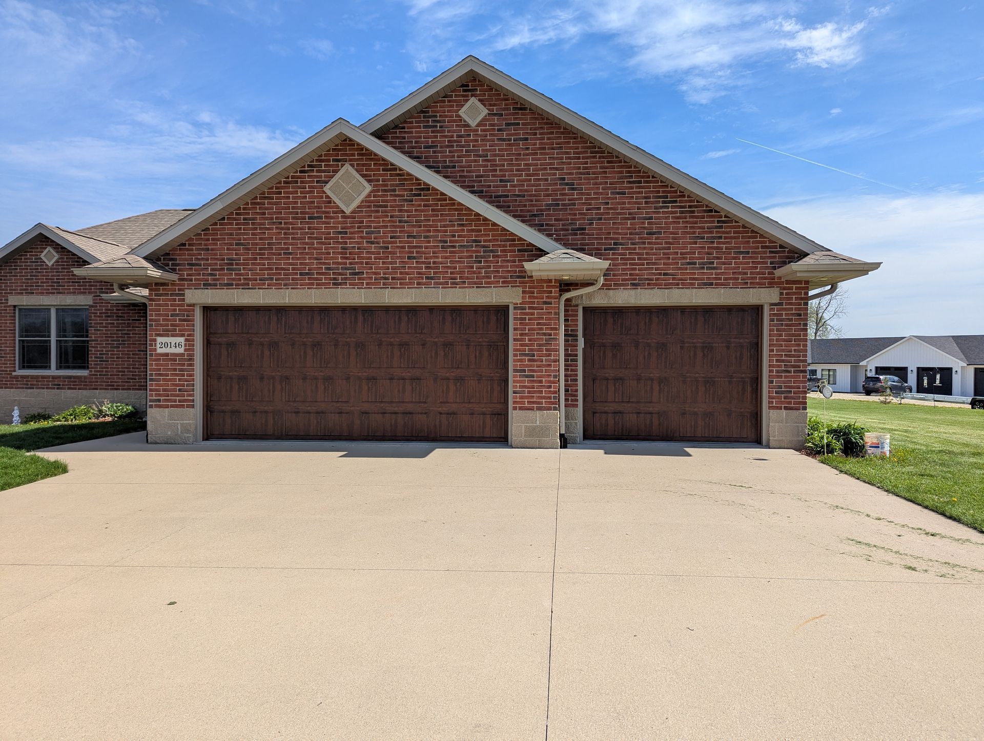 Brick suburban house with two-car garage and light concrete driveway under a blue sky