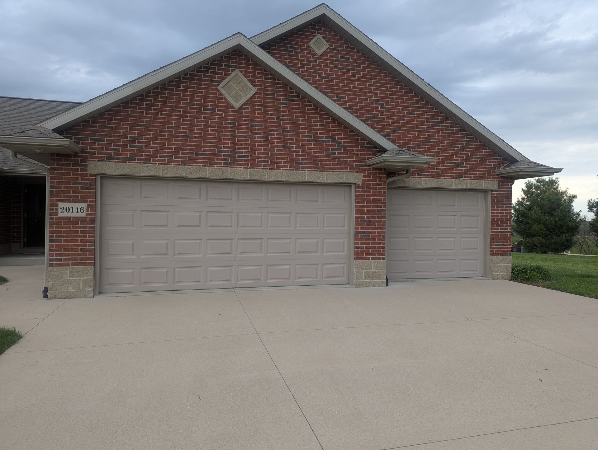 Brick suburban house with two-car garage and driveway under overcast sky