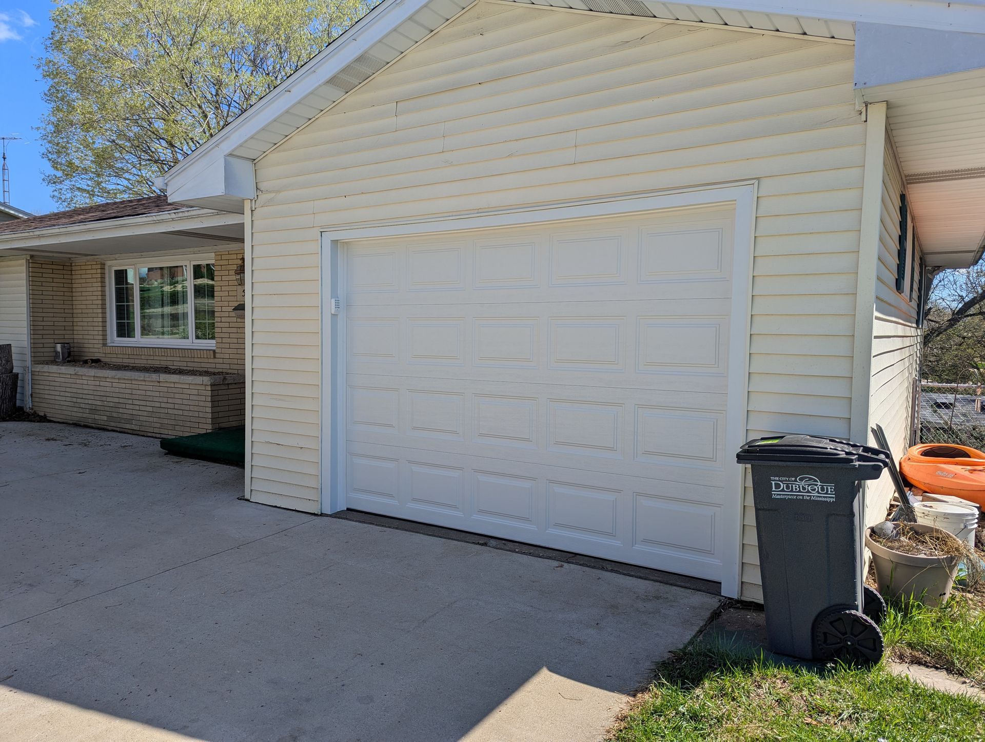 White garage door on a beige house with a driveway and a trash bin beside it