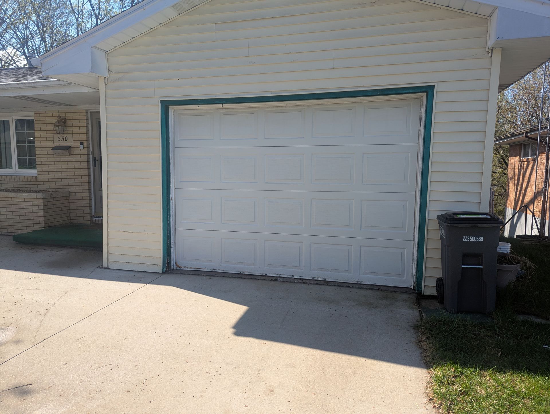 White garage with a closed door and trash bin beside it in a driveway.