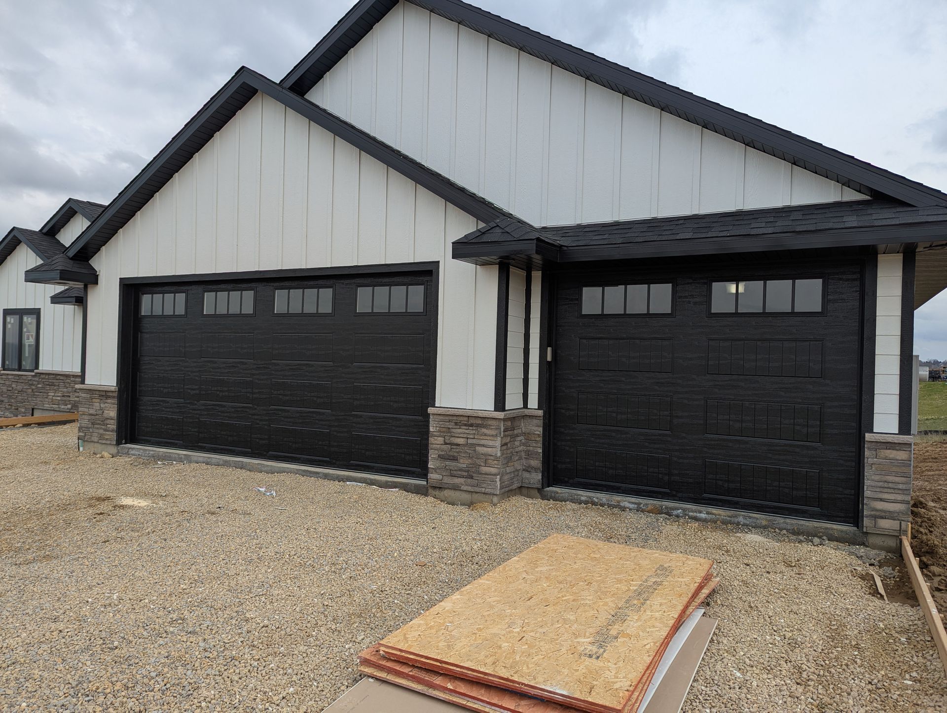 New white-and-black garage exterior with two dark doors and gravel driveway under construction