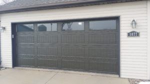 Two-car gray garage door on a white house with a concrete driveway and house number plaque beside it