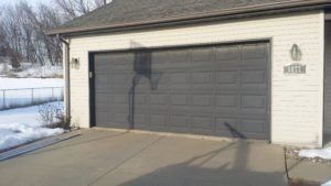 Detached garage with a closed gray door, snow on the ground, and a driveway in front.