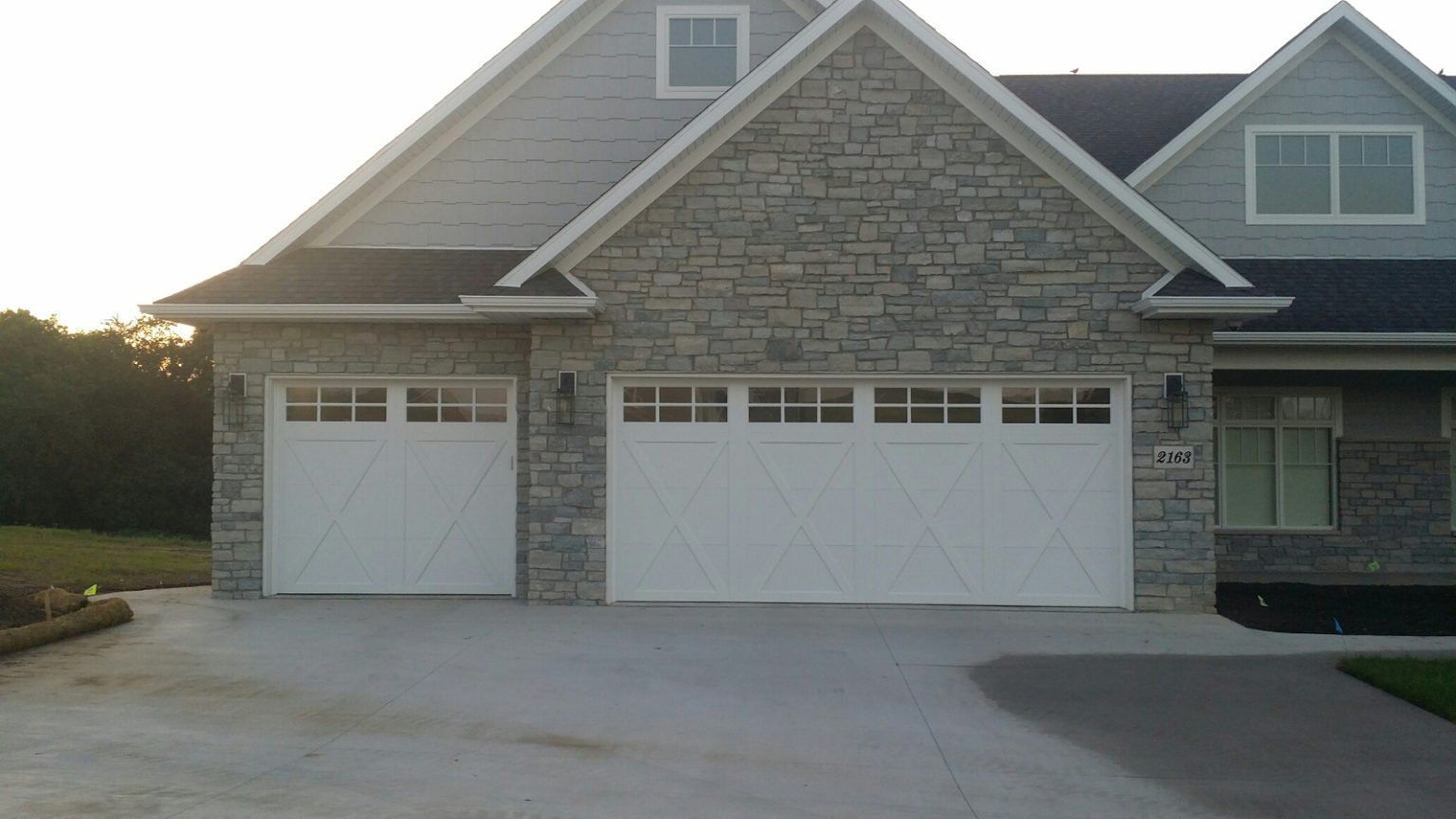 Two-car garage on a stone-front house with a concrete driveway at dusk