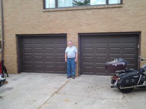 Man standing between two garage doors, with motorcycles parked on both sides.