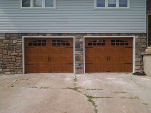 Two wooden garage doors in a stone-and-siding house exterior above a concrete driveway
