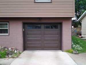 Brown garage door on a brick-and-siding house with a concrete driveway and small garden beds.