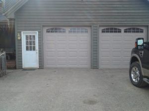 House garage with two beige doors, a white side door, and part of a black truck parked on the right.
