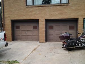 Two brown garage doors on a brick building, with a white vehicle at left and a motorcycle parked at right.
