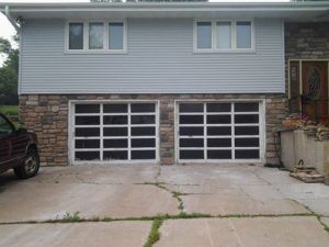 House with two white garage doors, stone facade, and cracked concrete driveway