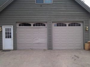Gray house facade with two beige garage doors, a side entry door, and a driveway