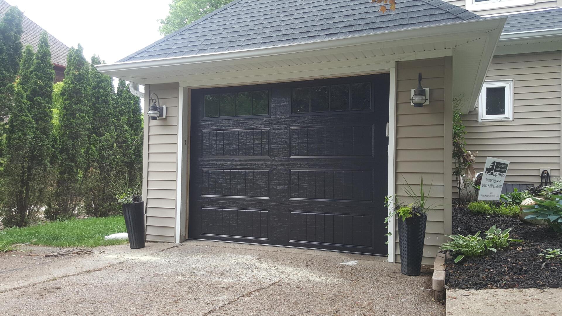 Detached garage with black double doors, beige siding, and a gravel driveway.