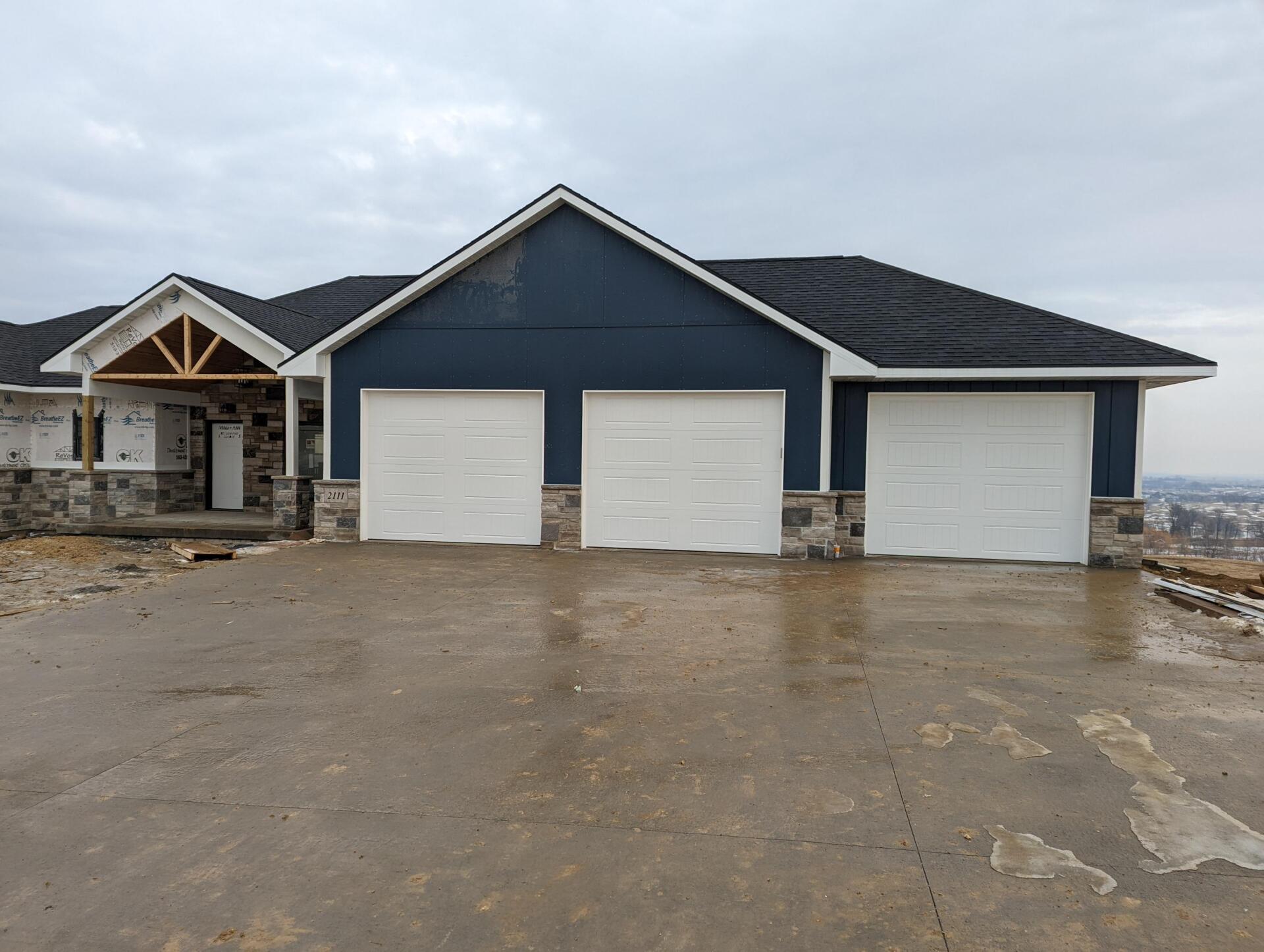 New house exterior with blue siding, stone accents, and three white garage doors
