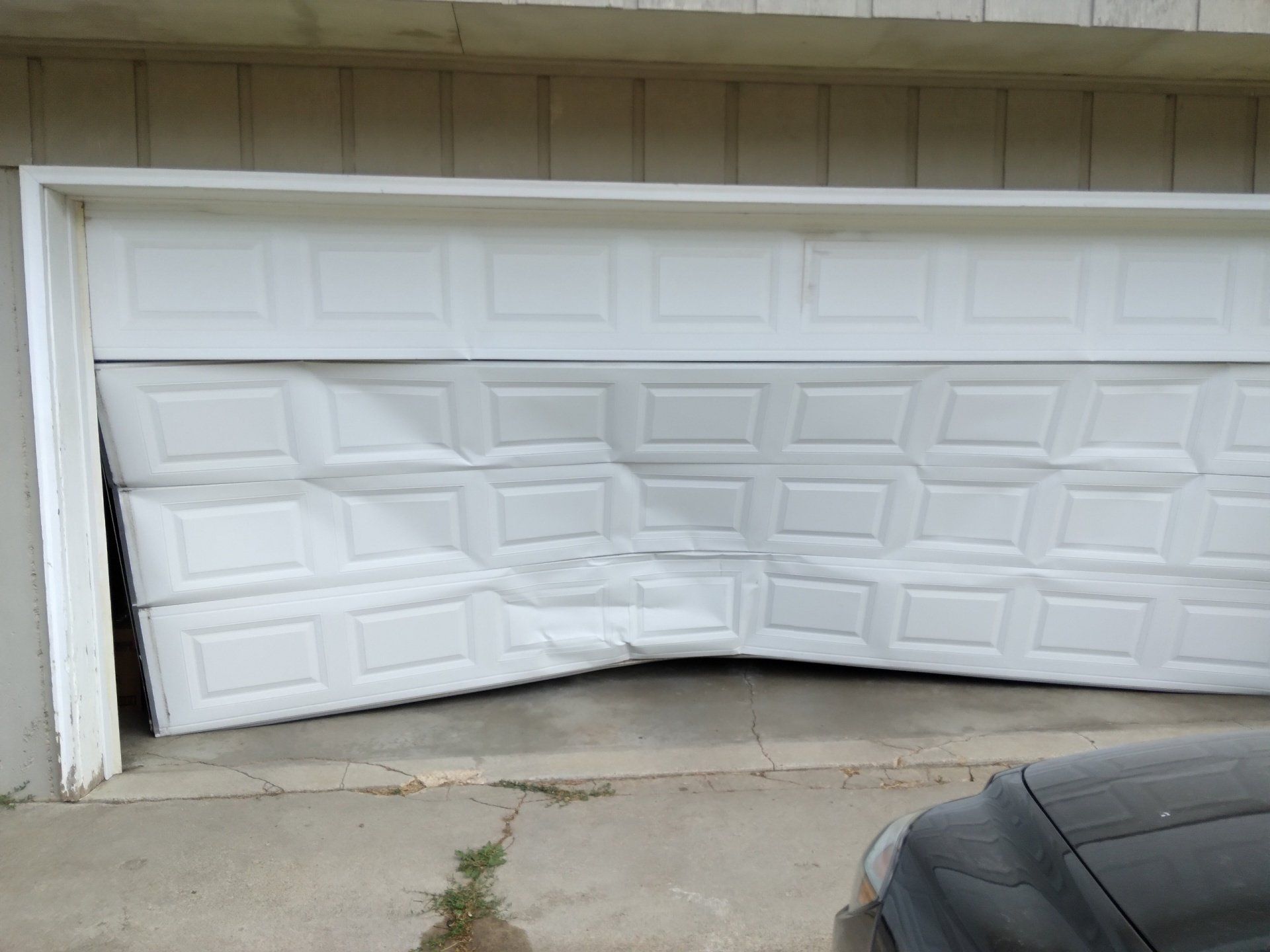 Bent garage door with a damaged lower panel and a car parked in front