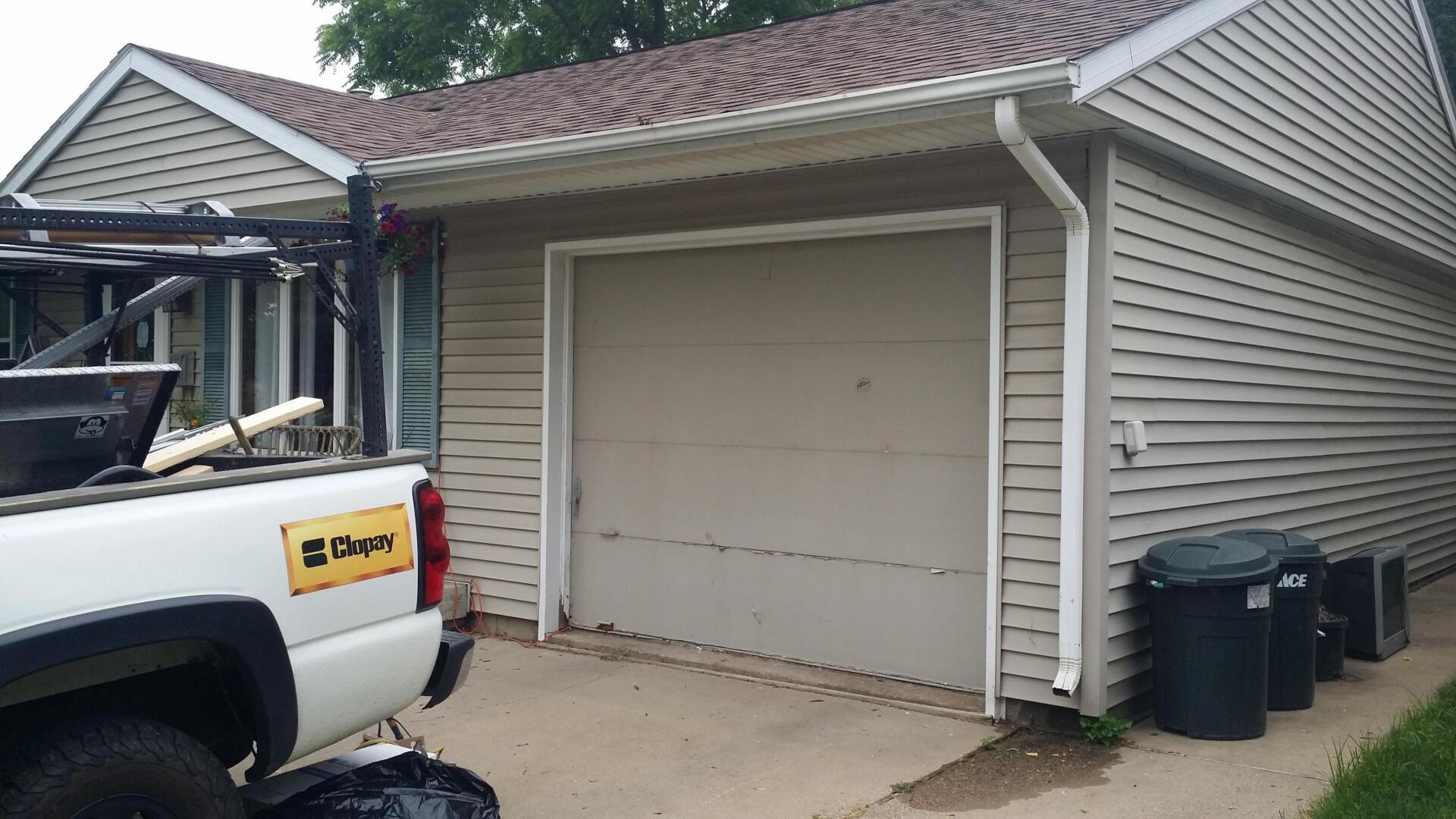 Suburban garage with beige siding, white trim, a parked pickup truck, and trash bins along the side.
