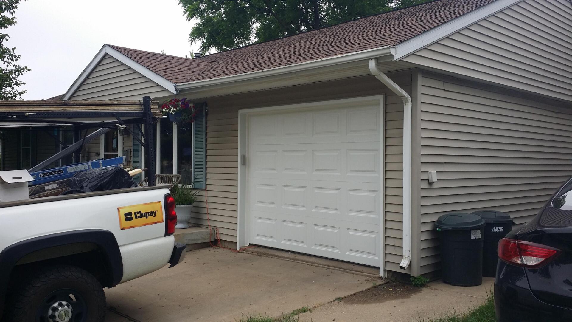 Suburban garage with white door, parked pickup truck, and trash bins beside the driveway