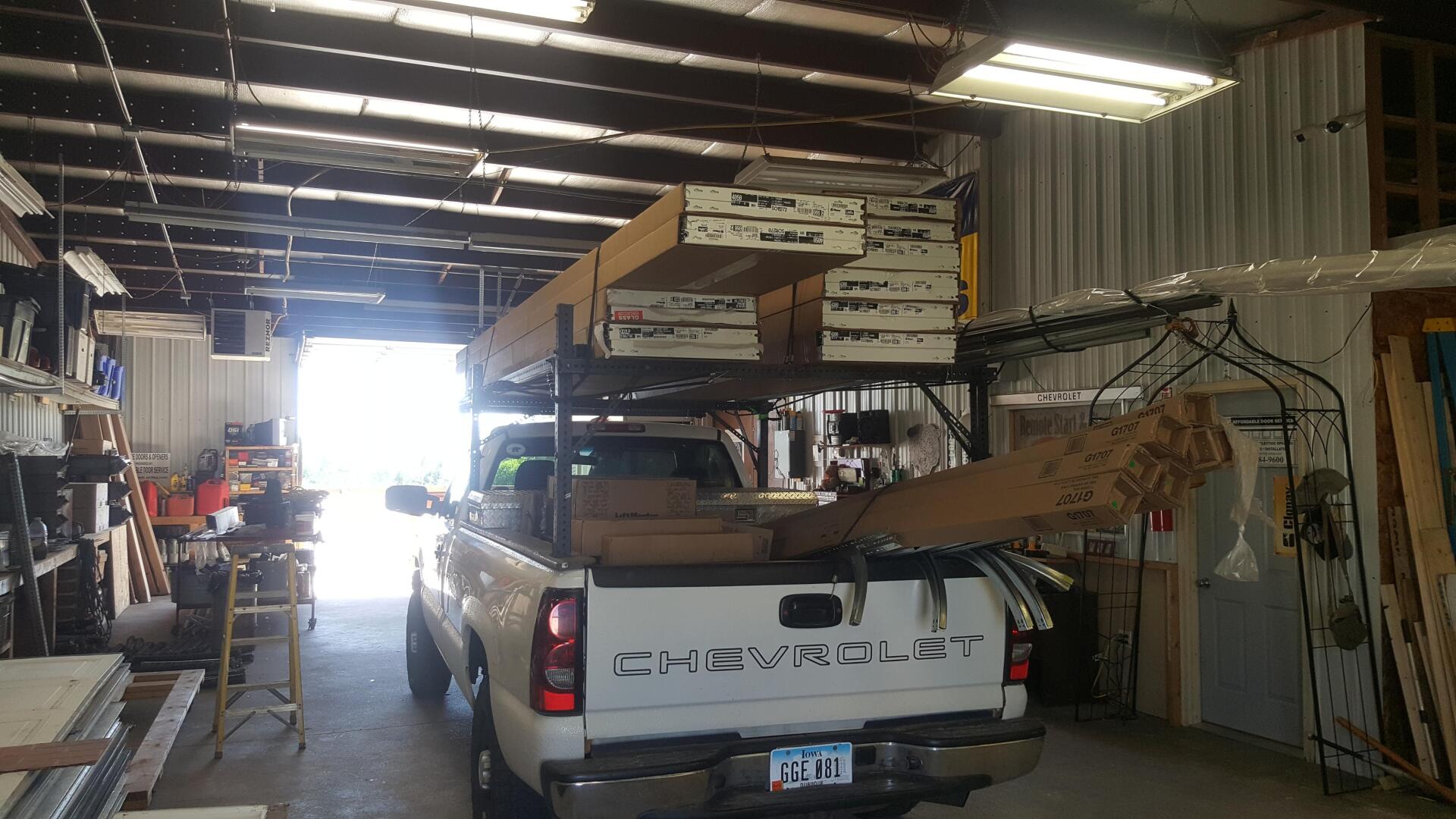 White pickup truck in a cluttered workshop or garage with stacked materials and equipment.