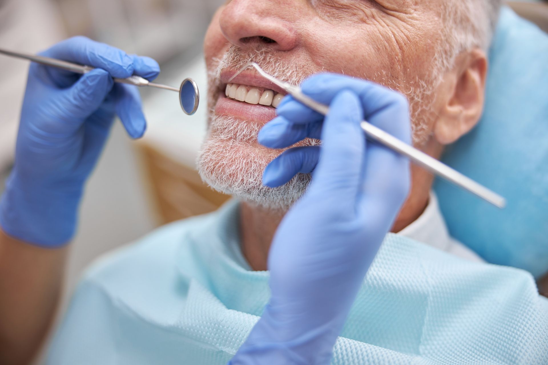 Dentist examining a patient’s teeth with dental tools and blue gloves