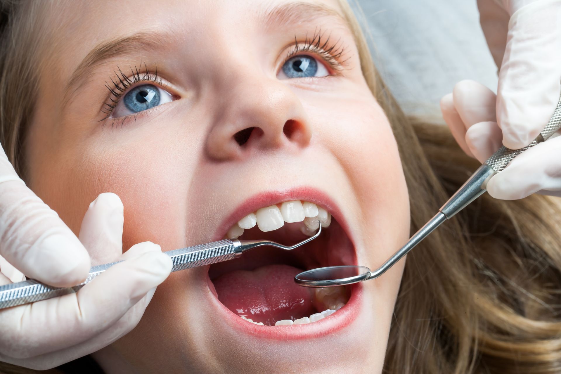 Child at the dentist with mouth open while tools examine teeth