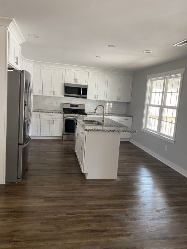 Bright modern kitchen with white cabinets, stainless appliances, island, and dark wood floors