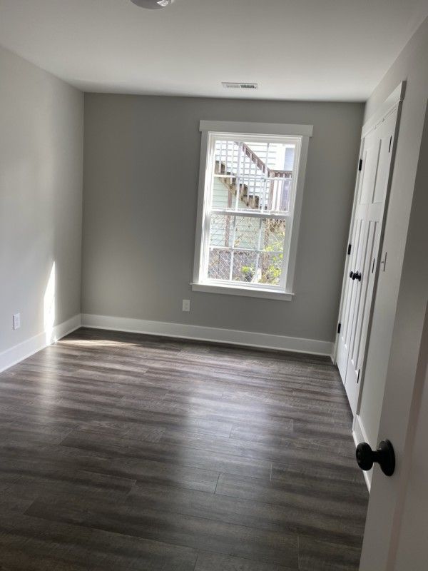 Empty gray bedroom with dark wood floors and a window showing outside stairs