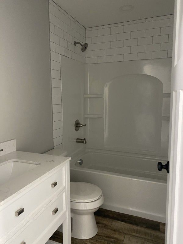 Small white bathroom with a toilet, vanity, and a tub/shower with subway tile and a glass panel.