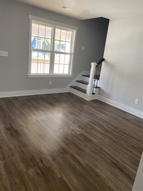 Empty living room with gray walls, wood floor, and a window by a small staircase.