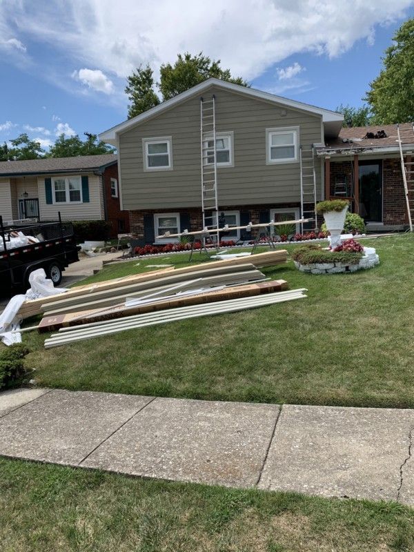 Backyard with stacked lumber on the lawn in front of a gray house under a blue sky