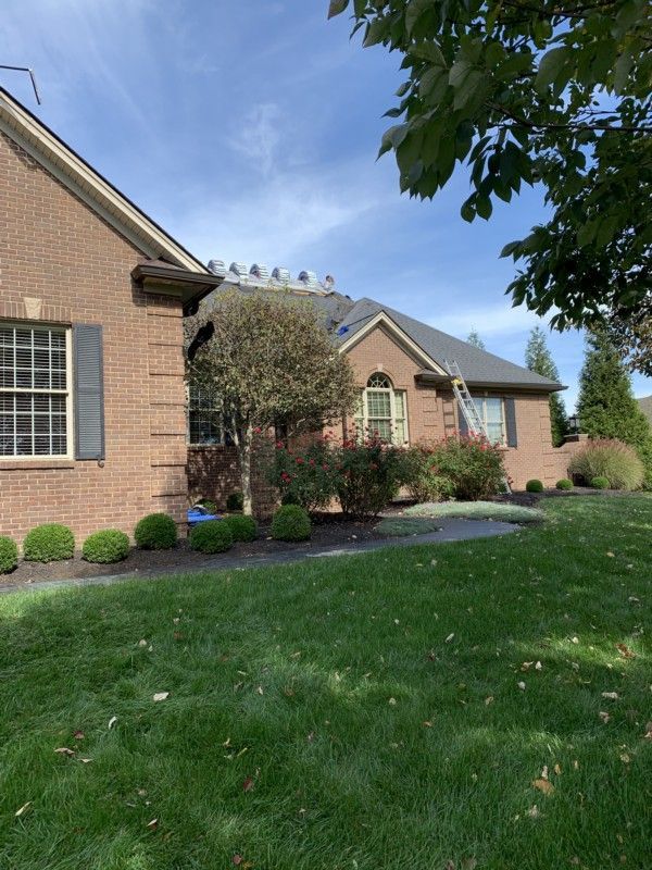 Brick suburban house with white-trimmed windows, manicured shrubs, and a green lawn under a blue sky