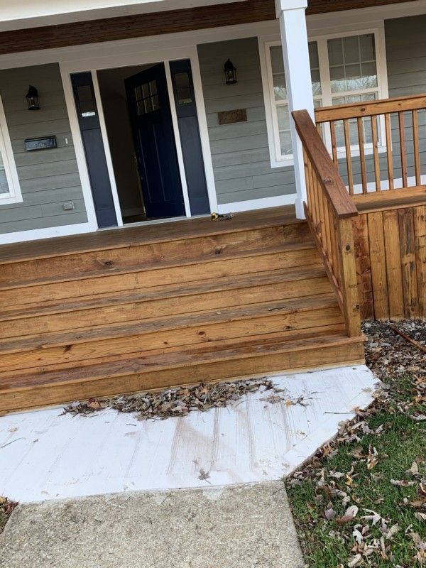 Front porch with wooden steps and railings, a black front door, and a white concrete walkway.