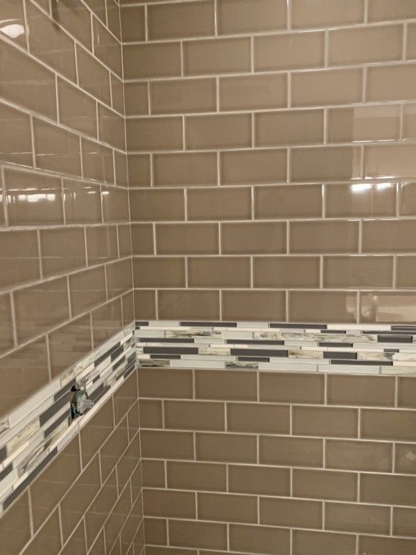 Corner shower with beige subway tile and a decorative gray-and-white mosaic border.