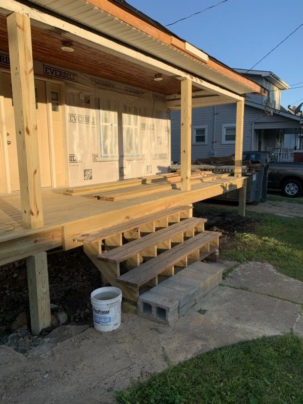 Partially built wooden porch and steps on a house with exposed framing and construction materials