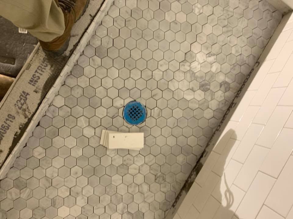 Tiled bathroom floor with a blue shower drain and a white rectangular access panel.