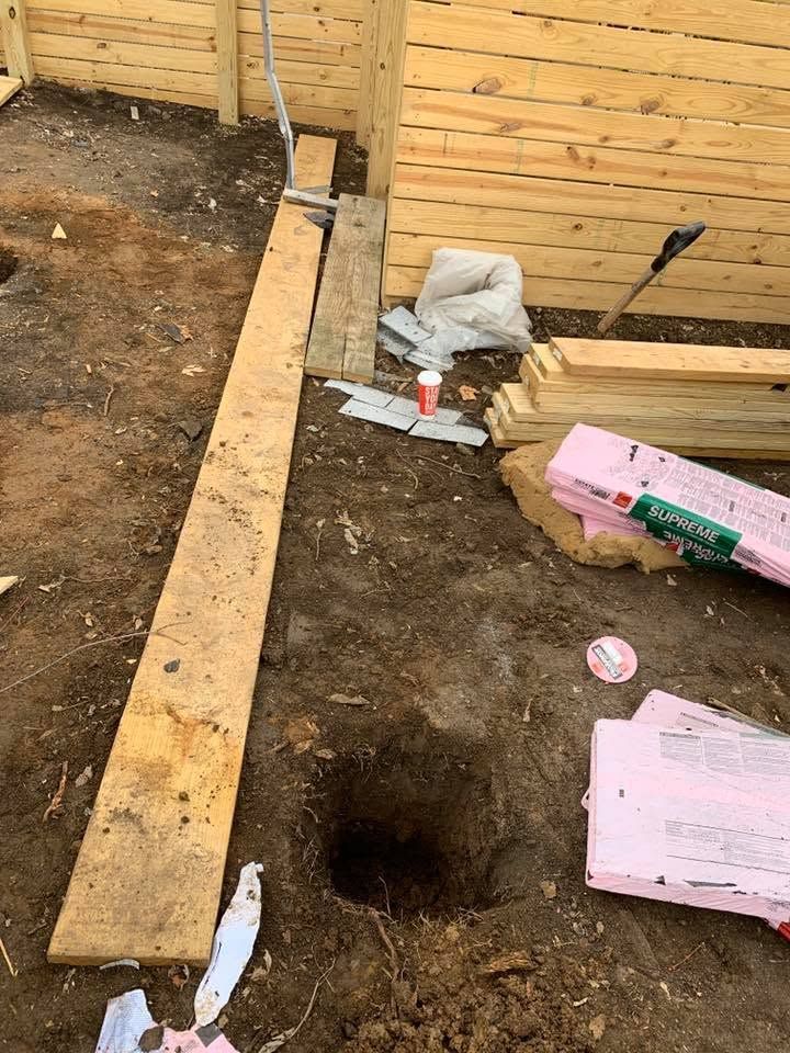 Construction site with wooden foundation beams, dirt trench, and tools near a wooden wall