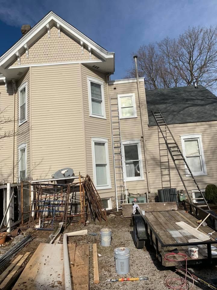 Tan house under renovation with scaffolding, ladders, and construction materials in the yard