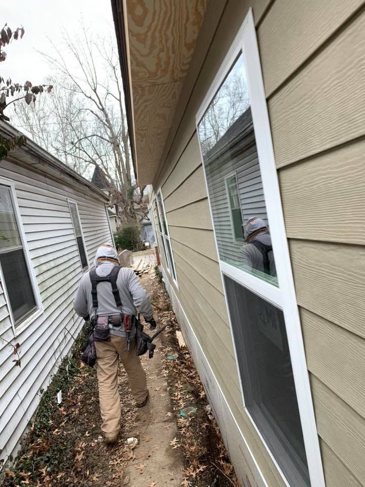 Worker carrying tools walks through a narrow outdoor passage beside houses on a cloudy day