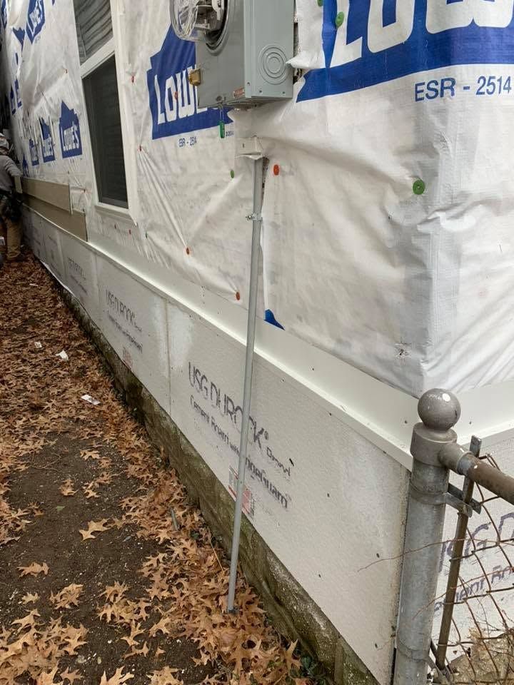 Wrapped house exterior with white siding and blue housewrap behind a chain-link fence.
