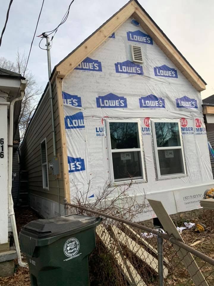House under renovation wrapped in Lowe’s house wrap, with white siding and a fenced yard