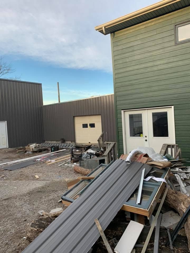 Construction debris piled beside a green building and gray garage in an industrial yard.