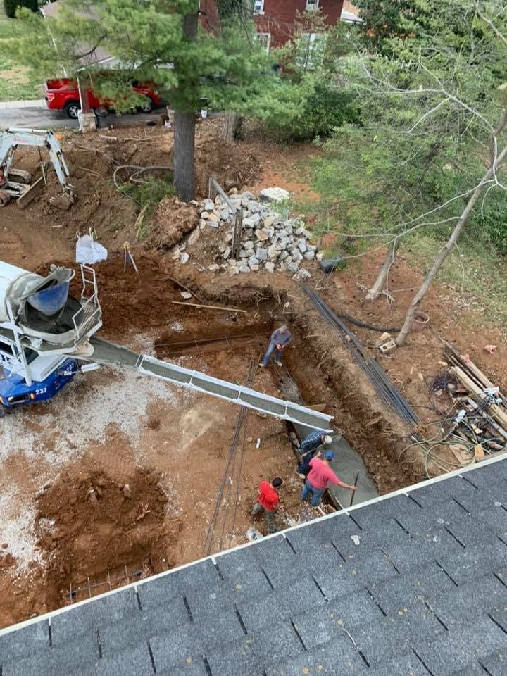 Construction workers digging a trench in a yard beside a house, with a concrete truck and exposed pipes.
