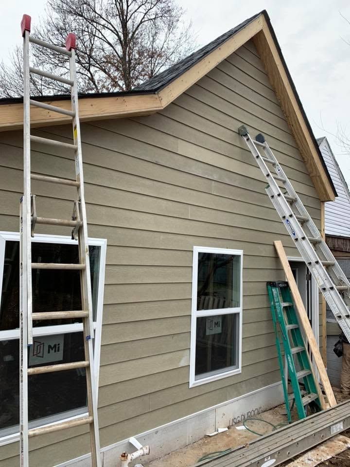 Ladders lean against a tan house exterior during roof and siding work.
