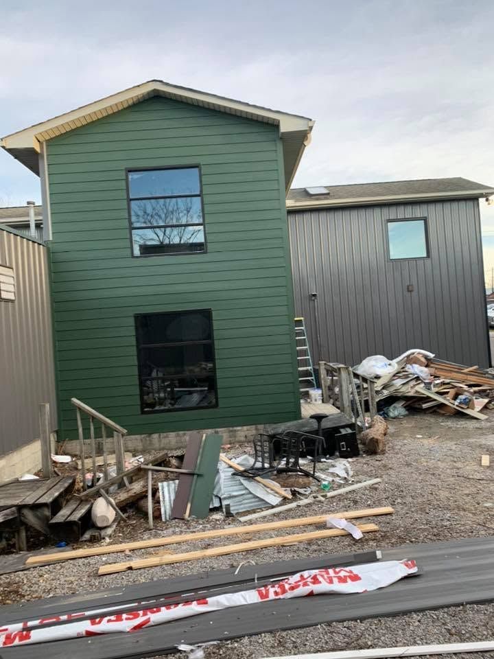 Green house exterior with damaged debris and construction clutter in the yard