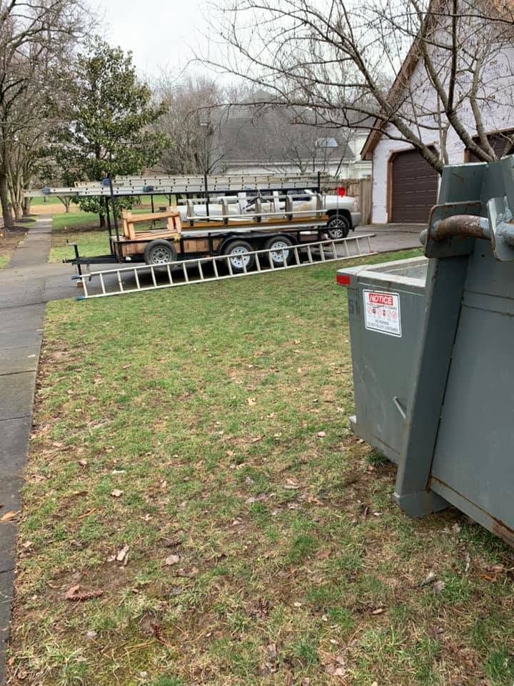 Ladders on a trailer parked beside a house, with trash bins and a grassy yard in the foreground