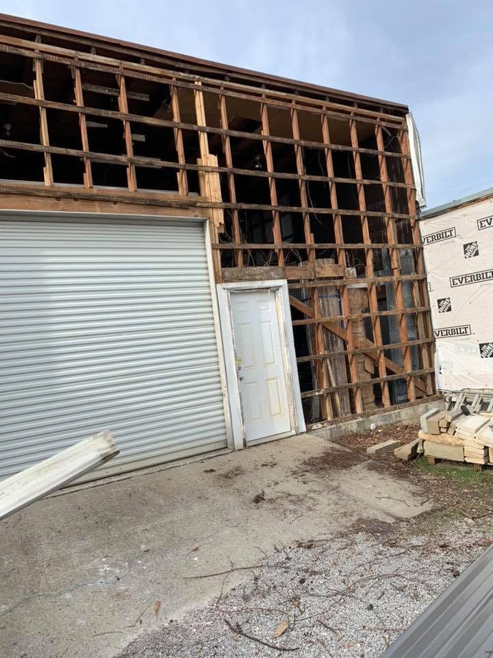 Partially demolished building with exposed wooden framing and a white roll-up garage door