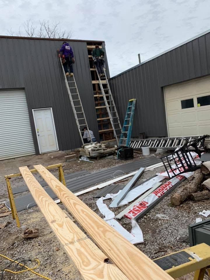 Workers on ladders repairing a building roof amid construction debris outdoors