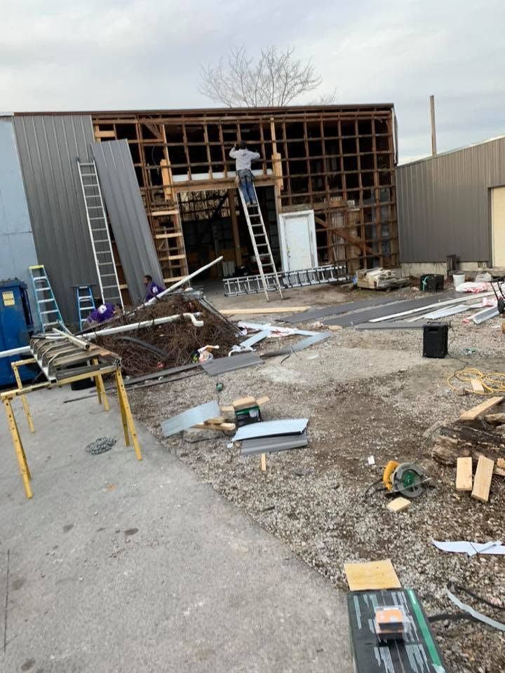 Damaged building exterior under renovation, with exposed framing, debris, ladders, and workers on site