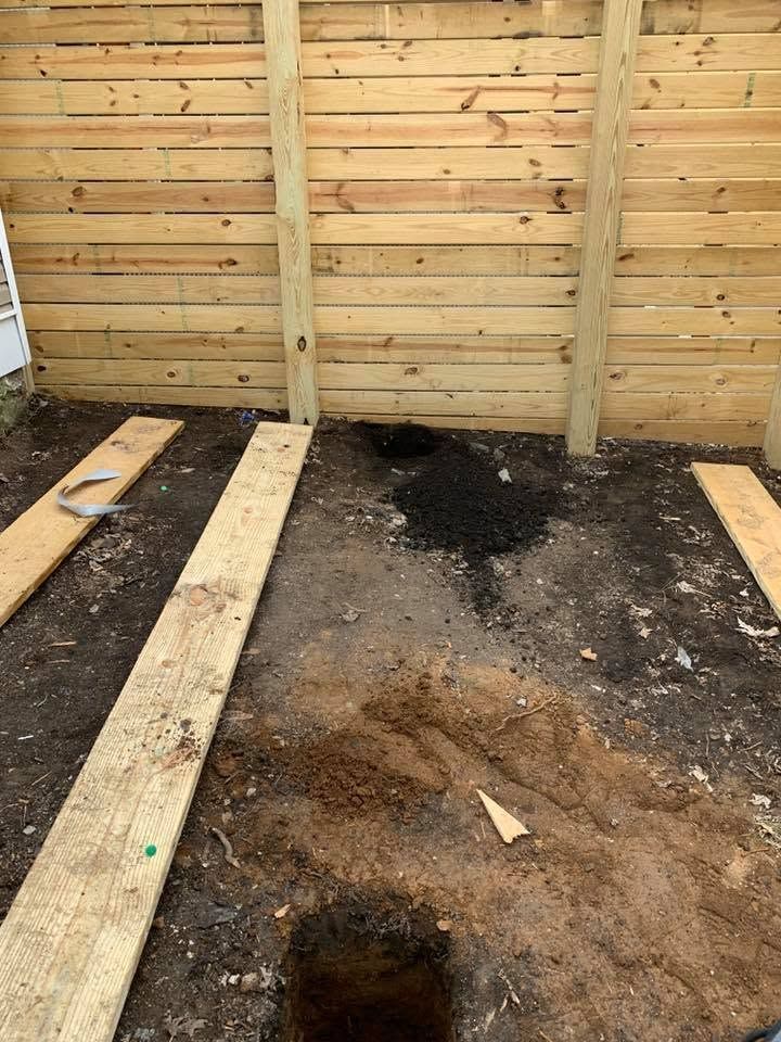 Wooden fence with a muddy, excavated ground area and several planks laid across it.