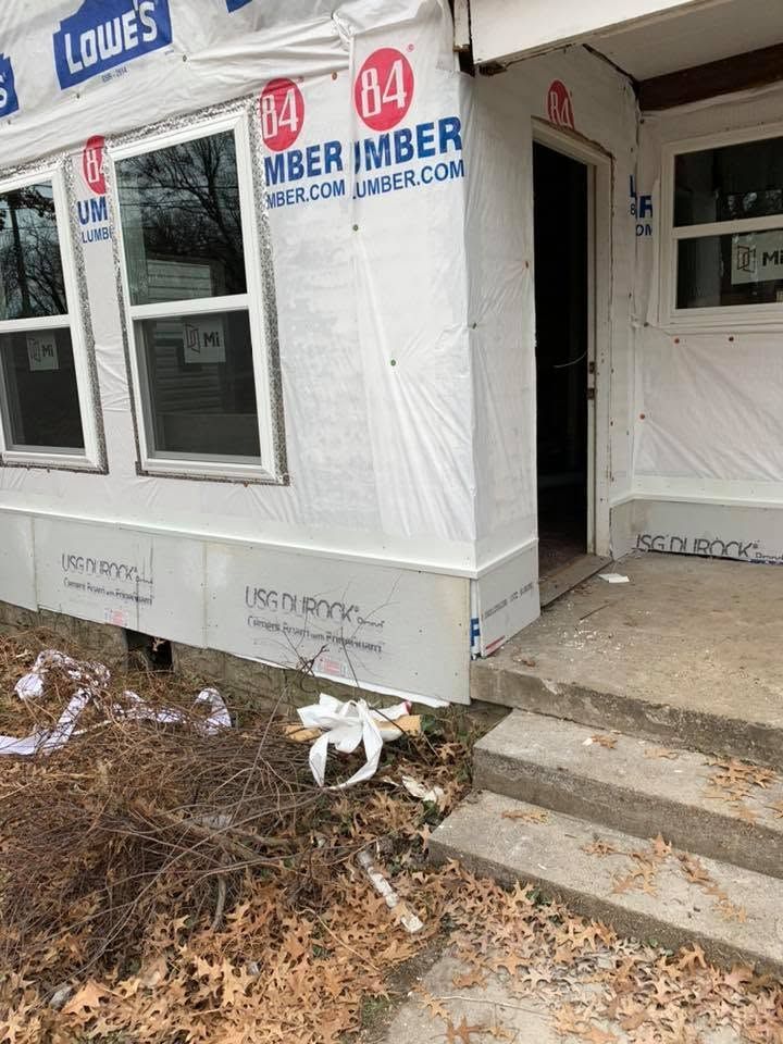 House under construction wrapped in white house wrap beside Lowe’s, with front steps and debris on the ground